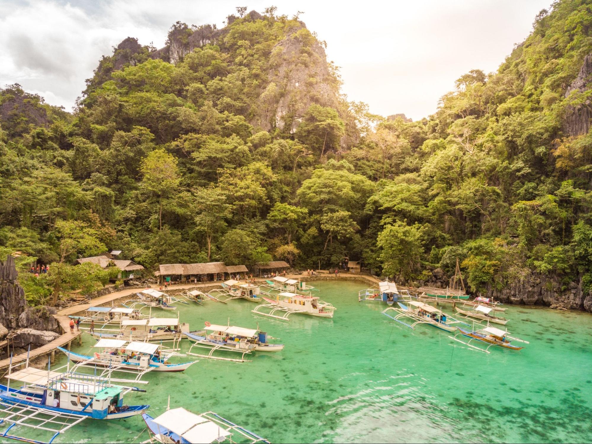 Blue crystal water in paradise Bay with boats on the wooden pier at Kayangan Lake in Coron island