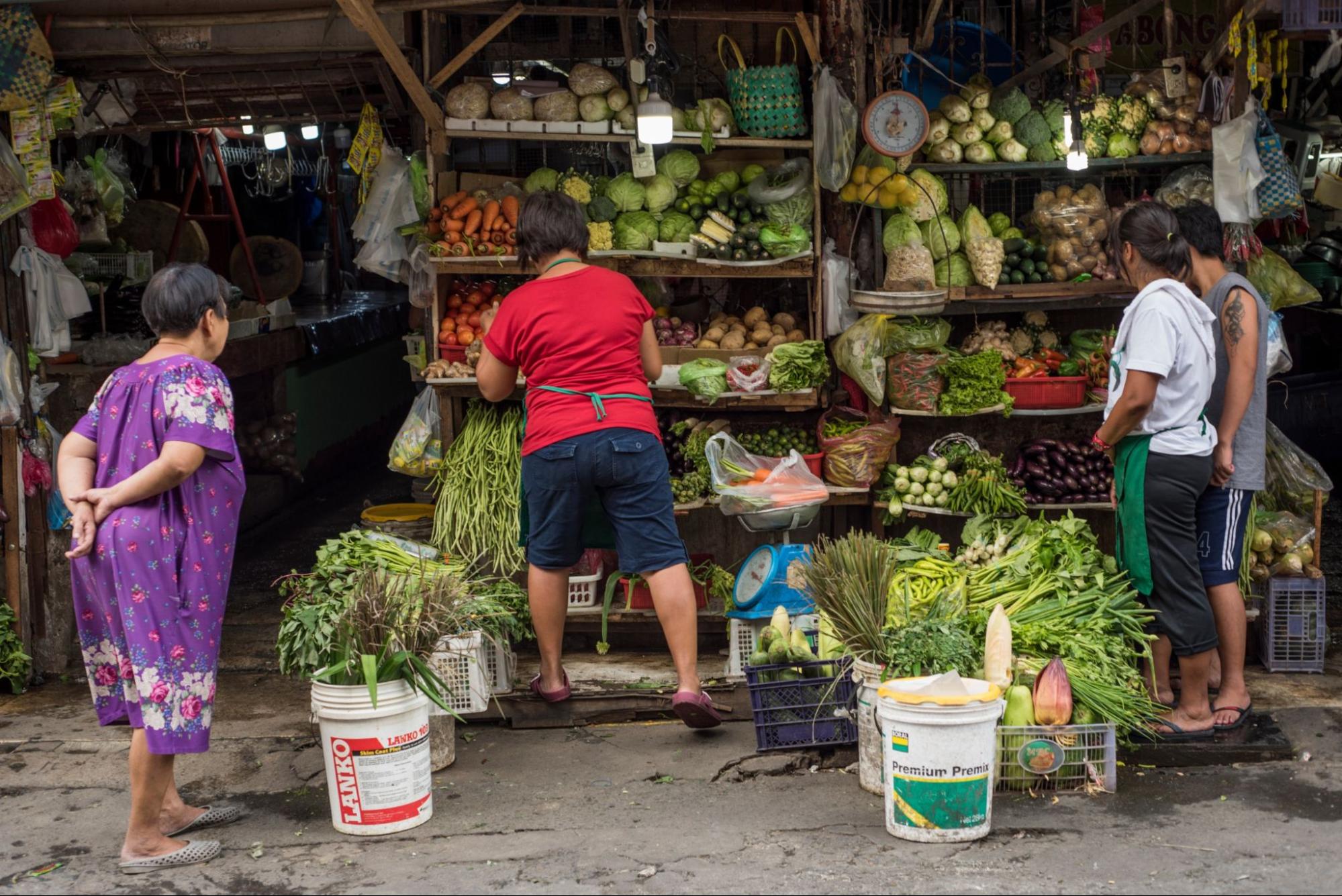 Customers buy fruits and vegetables in a street grocery shop in Manila