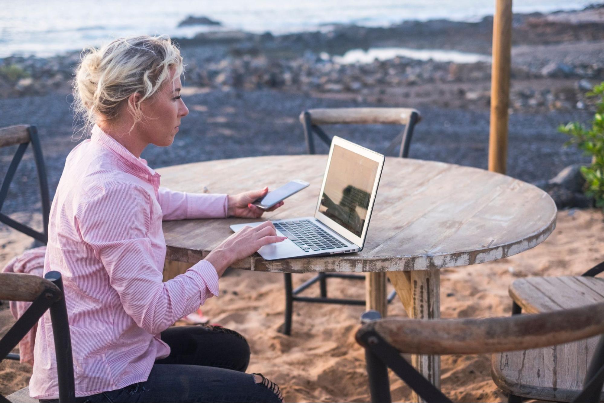 digital nomad , Woman working at the laptop and sitting on a wood table near the ocean